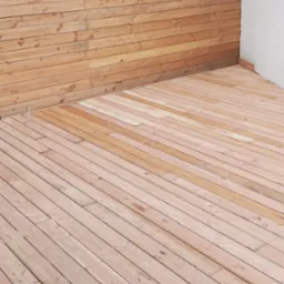 Drewniany taras z deskami ułożonymi pod kątem, przylegający do ściany z drewnianą boazerią i oknem w stanie surowym.