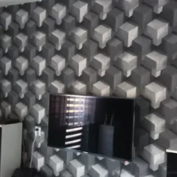 Pokój z szarą ścianą i tapetą w geometryczne wzory 3D, na ścianie wiszący zegar i telewizor, na szafkach lampka nocna i zegarek.