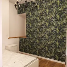 Wykończona sypialnia z tapetą w tropikalne liście, drewnianą podłogą, białym łóżkiem z folią ochronną i czarnym żyrandolem.