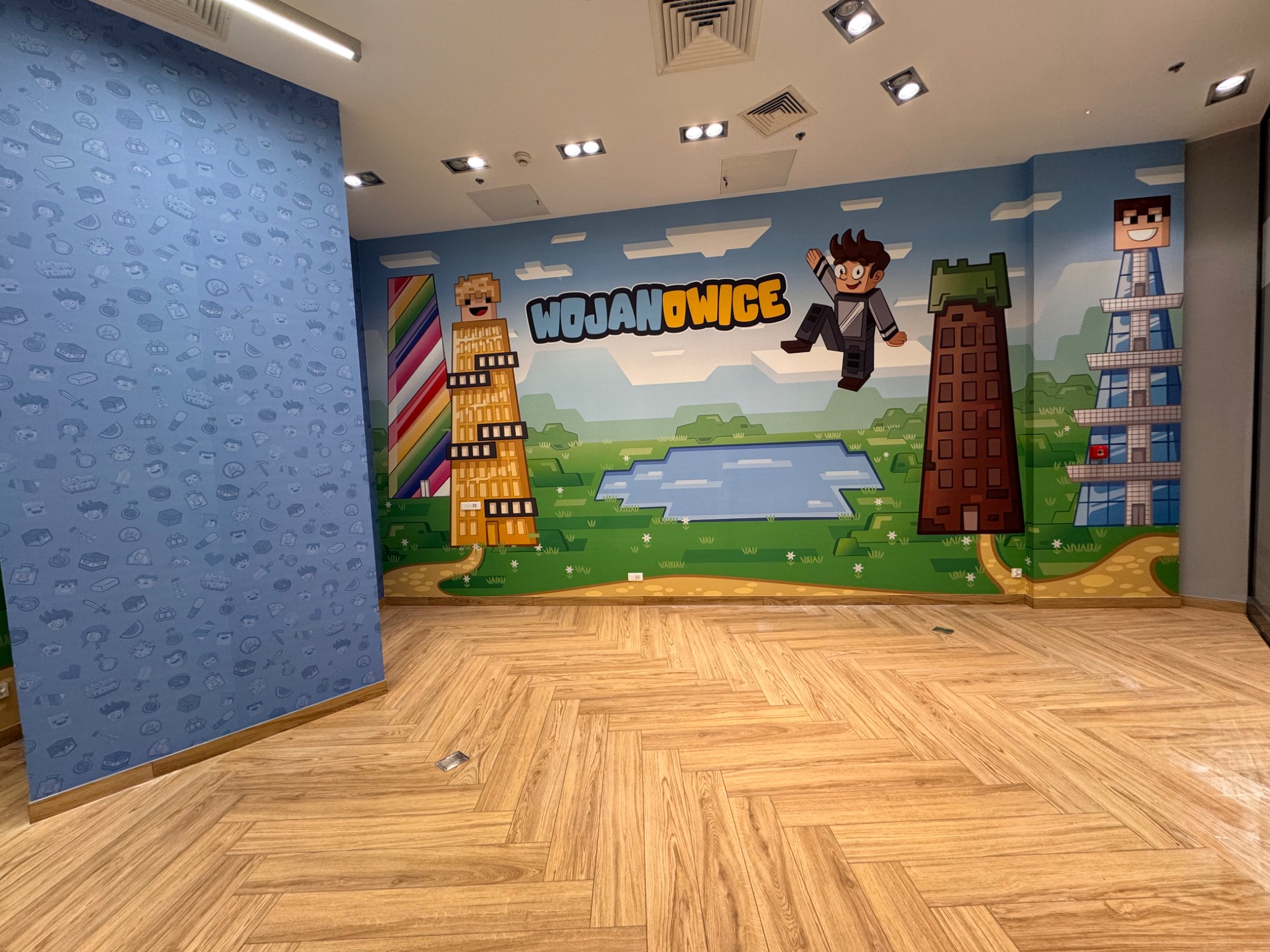 Pokój z tapetą w dziecięcym stylu z motywami Minecraft i nazwą Wojanowice, drewniana podłoga w jodełkę. Nietypowe wzornictwo.