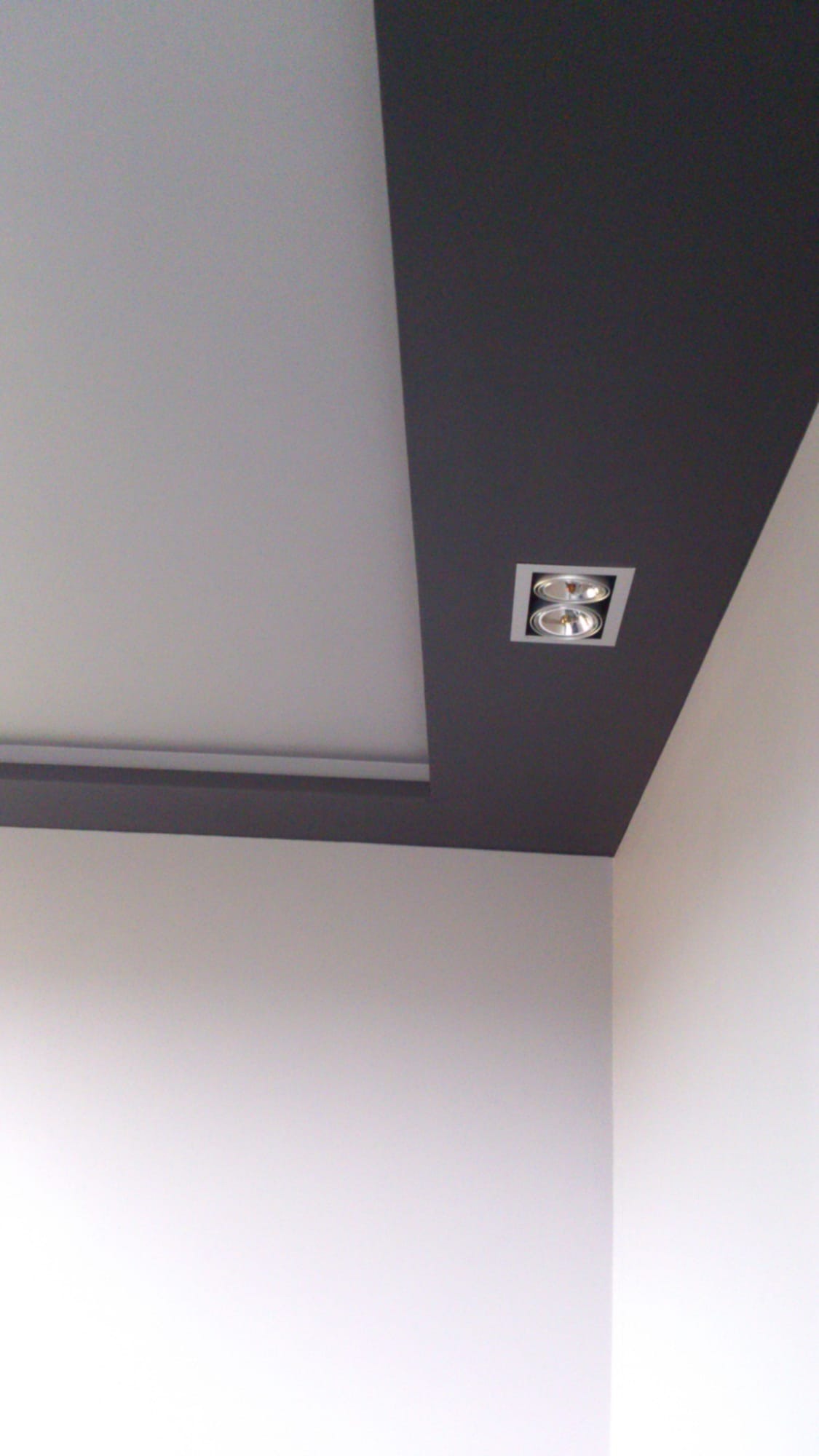 Nowoczesny sufit podwieszany z wbudowanym oświetleniem punktowym, pomalowany na biało i grafitowo, z widocznym narożnikiem ściany.