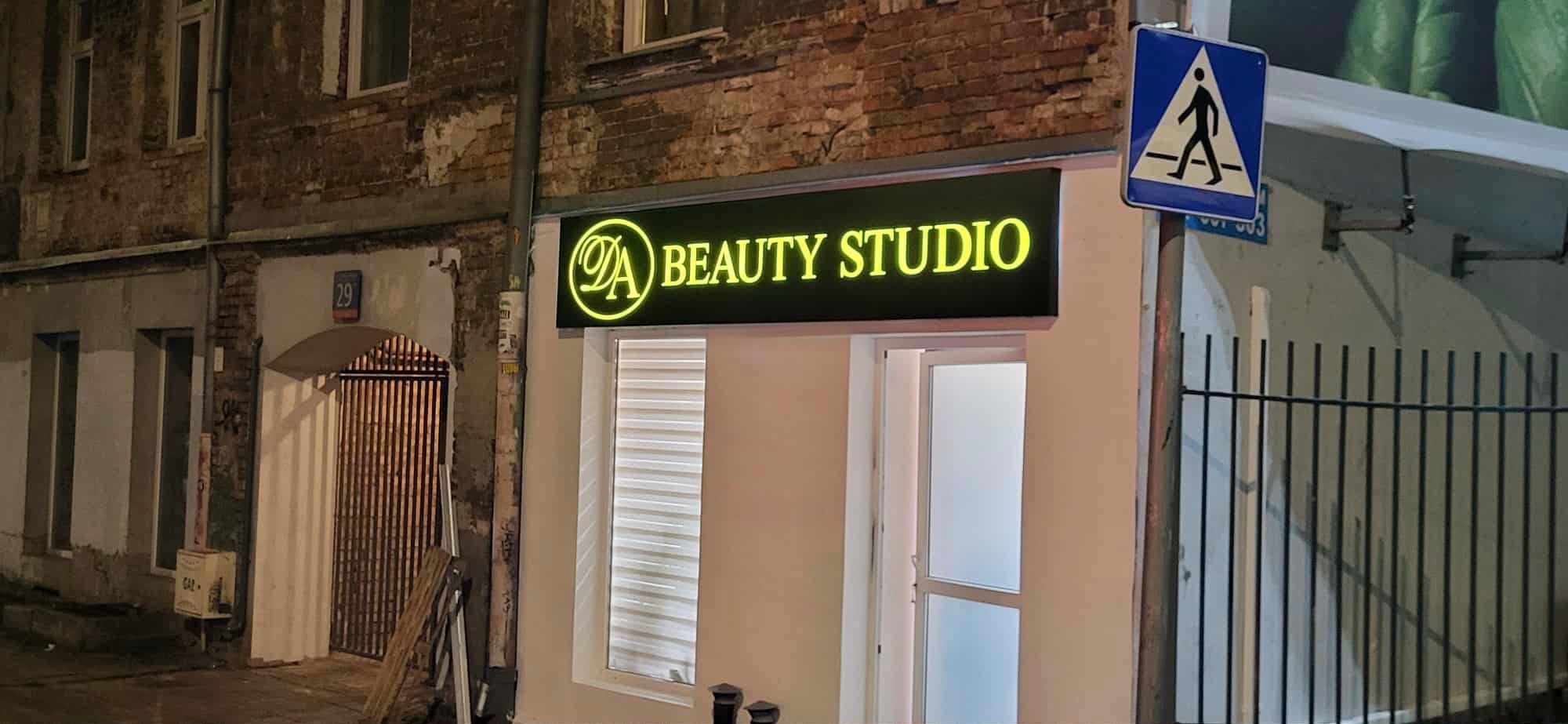Fasada budynku z szyldem 'Beauty Studio' podświetlonym na żółto, widoczny numer budynku 29 i znak przejścia dla pieszych. Ujęcie z ulicy.