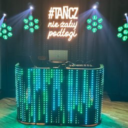 Dj Rafi Thomas Band - Oświetlona konsola DJ-a z neonowym napisem '#TANCZ nie żałuj podłogi', głośniki RCF i reflektory tworzą klubową atmosferę. Laptop na konsoli.