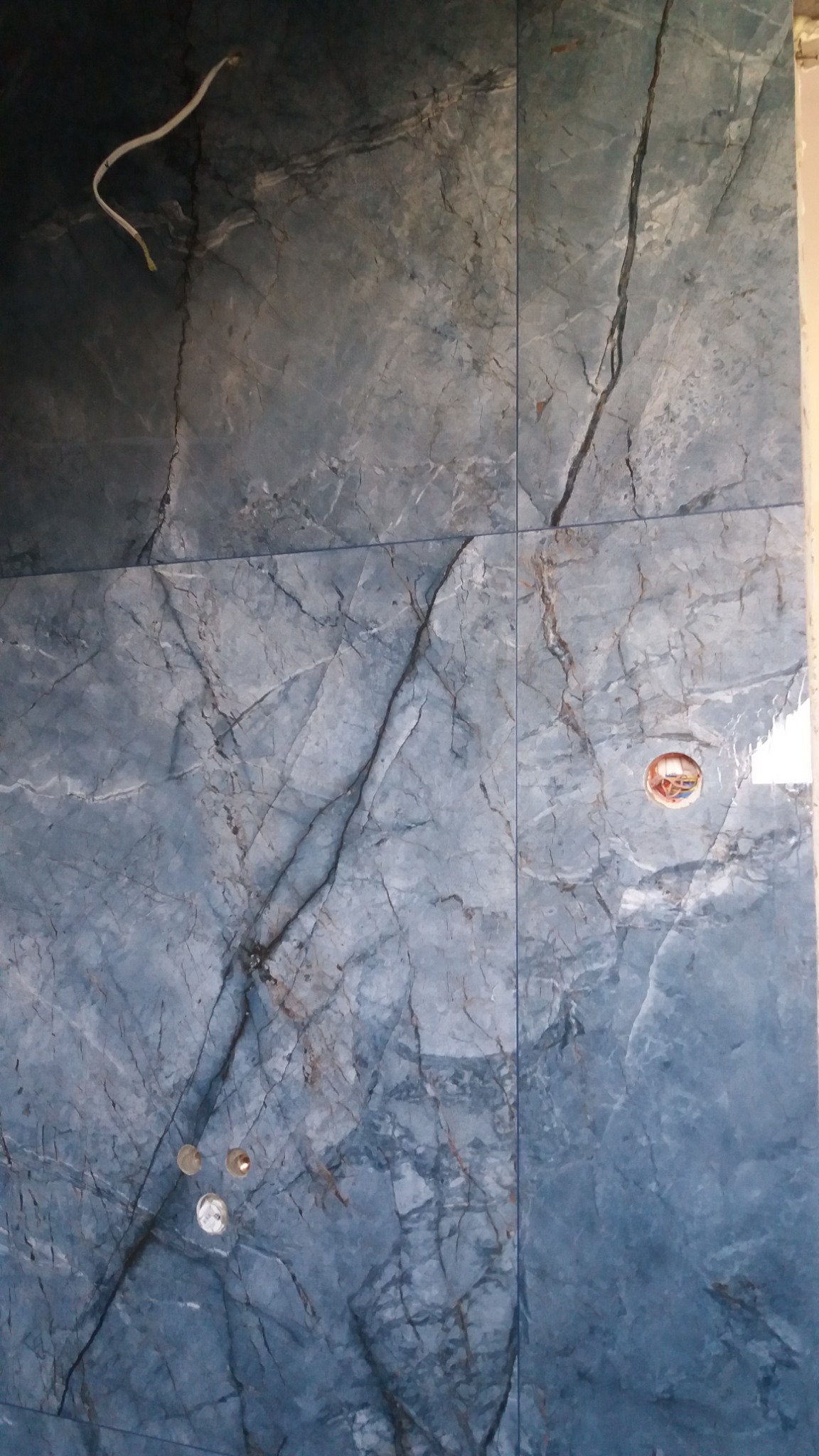 Ściana wyłożona niebiesko-szarymi płytkami imitującymi marmur w trakcie montażu instalacji elektrycznej w Nowym Sączu, widoczne otwory na gniazdka.