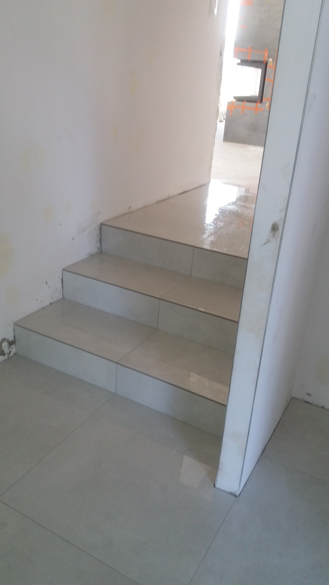 Schody wyłożone jasnymi, błyszczącymi płytkami w trakcie prac wykończeniowych; widoczne niedoskonałości na ścianie i podłodze.