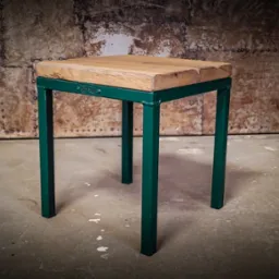 Drewniany blat na zielonym metalowym stelażu, wykonany w stylu loftowym w Jelcz-Laskowicach, na tle metalowej ściany z nitami.