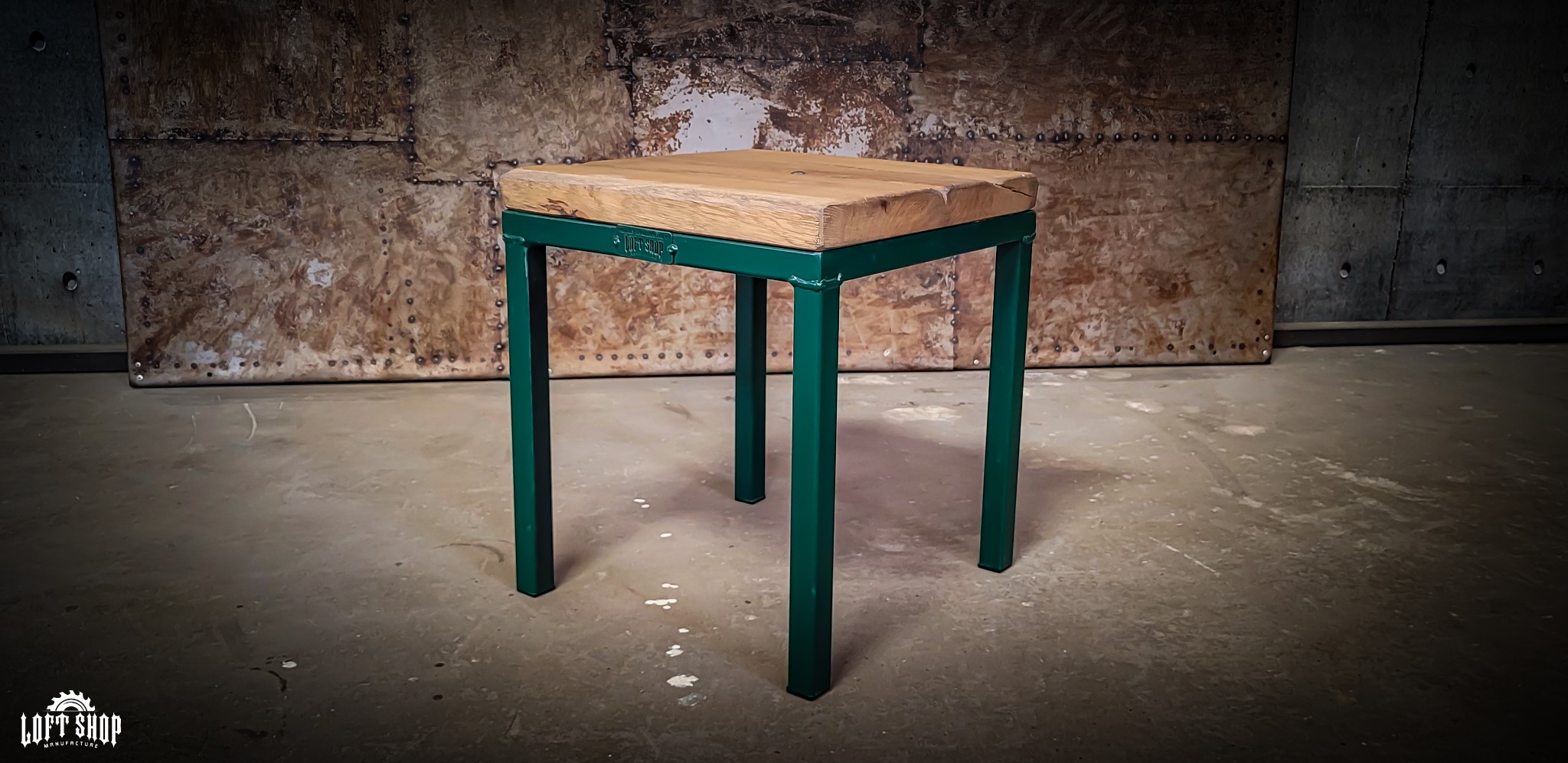 Drewniany blat na zielonym metalowym stelażu, wykonany w stylu loftowym w Jelcz-Laskowicach, na tle metalowej ściany z nitami.