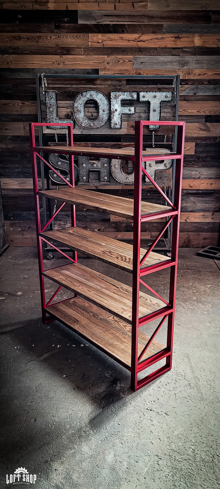 Regał w stylu loft z czerwonym metalowym stelażem i drewnianymi półkami z wyraźnym usłojeniem, na tle ściany z desek i dekoracji z napisem 'LOFT SHOP'.