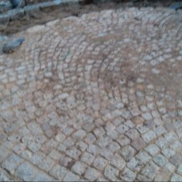 BrukPol Wiesław Kraiński - Niedokończona nawierzchnia z kostki granitowej ułożonej w łukowaty wzór, widoczne narzędzia murarskie i fragmenty niezabudowanego terenu.