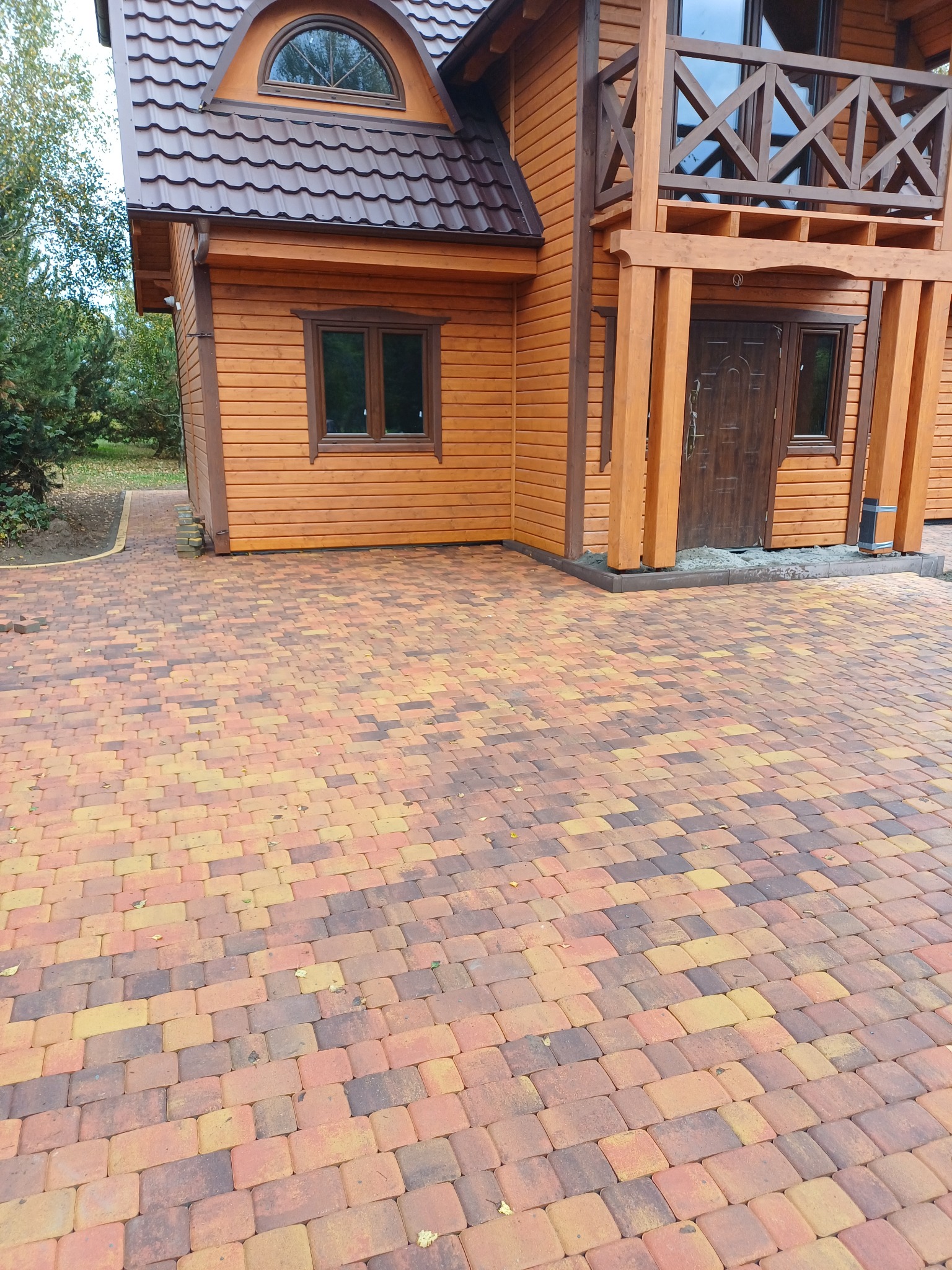 Kolorowa kostka brukowa prowadząca do drewnianego domu z brązowymi oknami i dachem, widok z perspektywy pieszego.