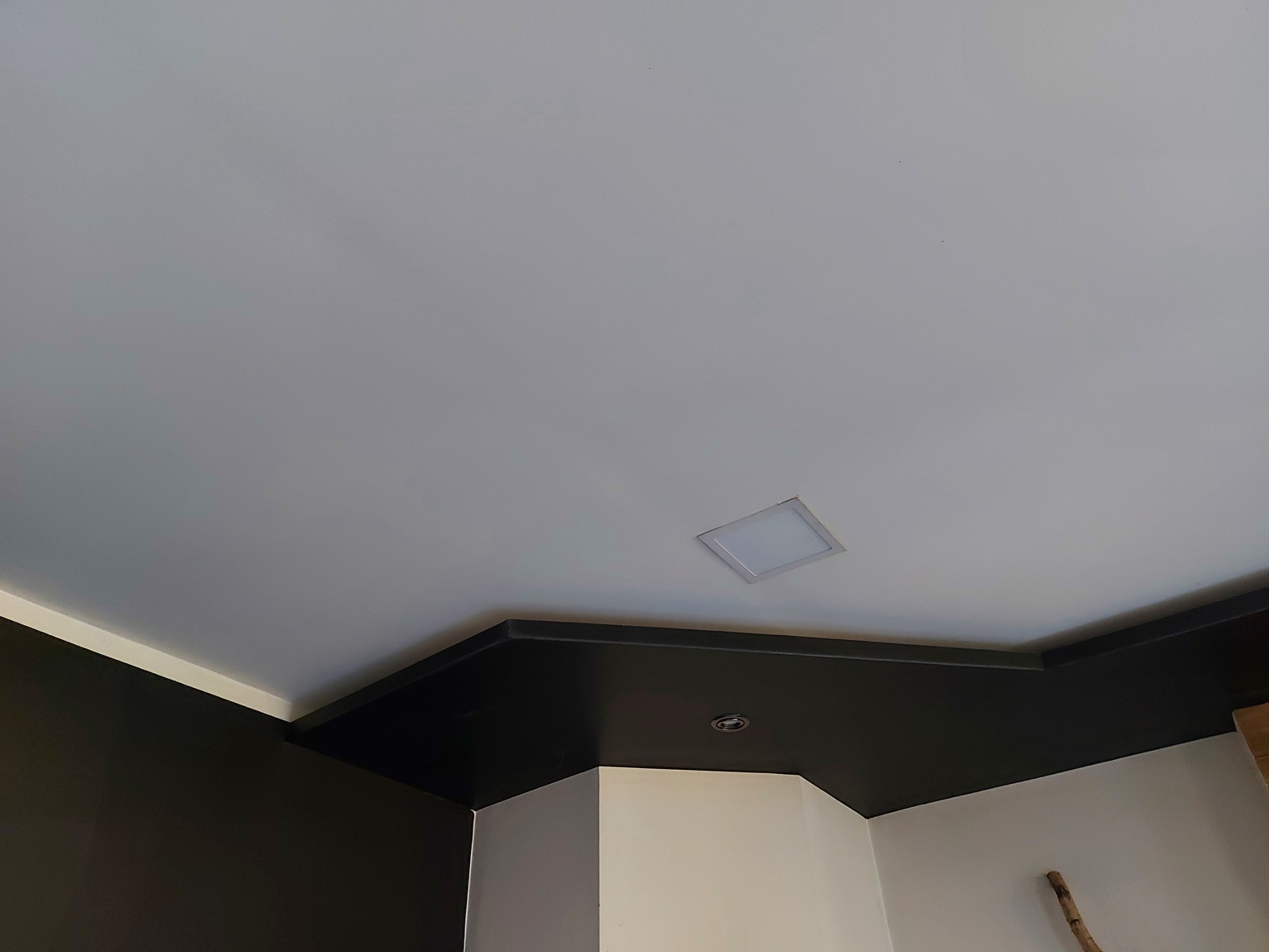 Pomieszczenie po malowaniu: biały sufit z nowoczesnym oświetleniem LED, czarny pas sufitowy i fragment ściany pomalowanej na ciemny kolor.