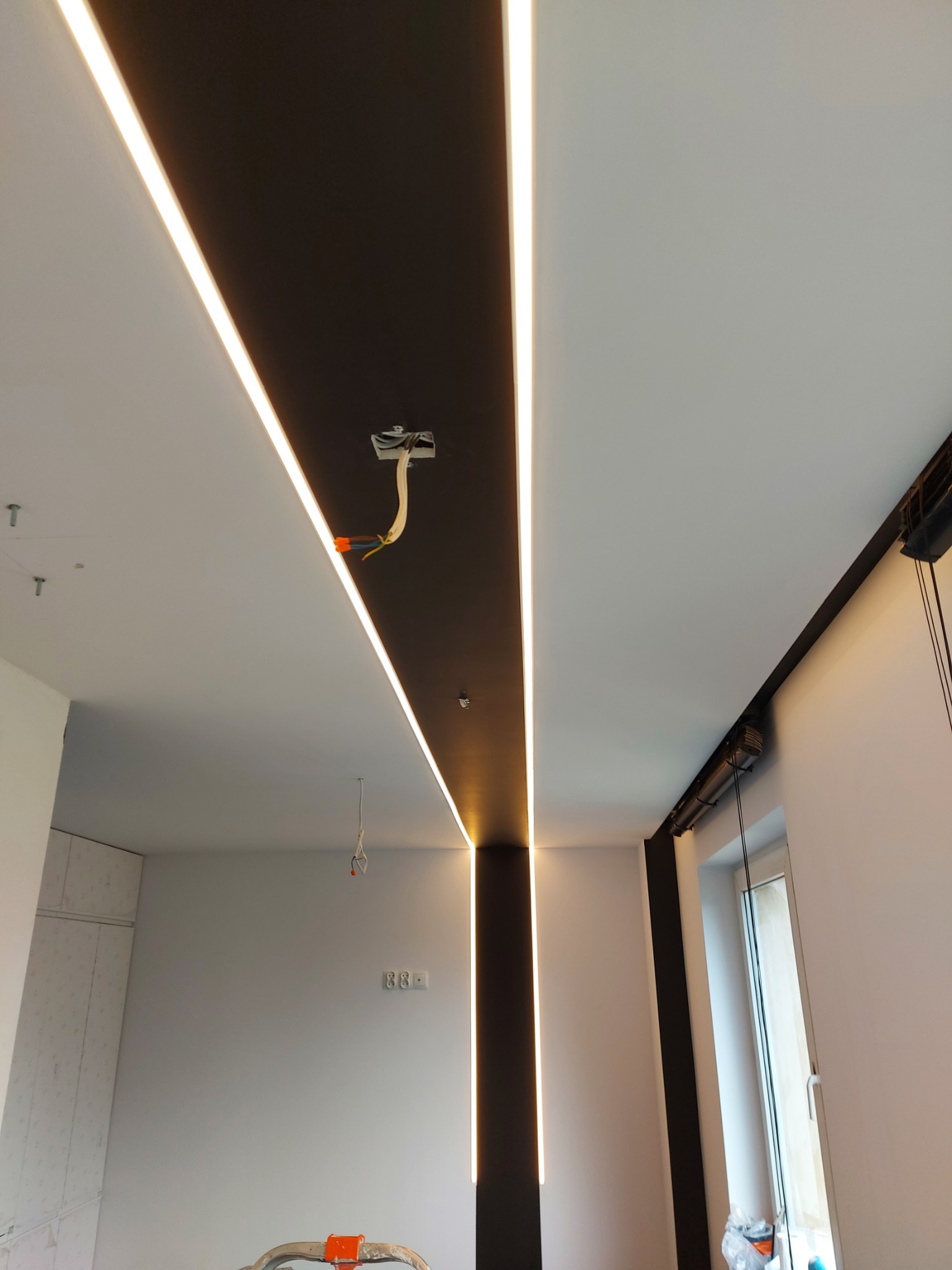 Nowoczesne oświetlenie sufitowe z liniowymi lampami LED w czarno-białym wnętrzu, widoczne przewody elektryczne w miejscu montażu lampy.