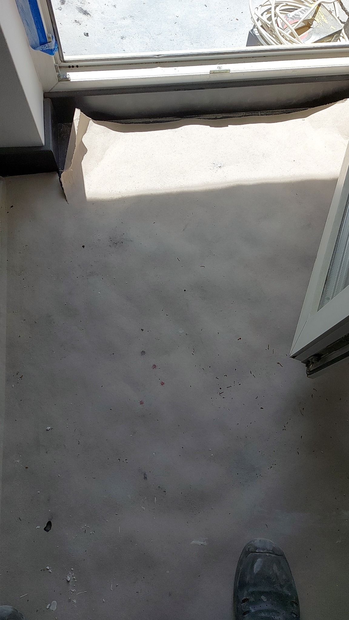 Przygotowany podkład podłogowy w trakcie prac wykończeniowych, widoczne zabezpieczenie folią i fragment buta pracownika.