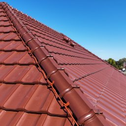 KWR Perun - Czerwona dachówka ceramiczna z zamontowanym systemem ochrony odgromowej, widok z góry na tle błękitnego nieba i zabudowań.