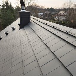 KWR Perun - Ciemnoszara dachówka z zamontowanymi uchwytami i przewodami systemu ochrony przed wyładowaniami atmosferycznymi, widok z góry na tle zabudowań i drzew.
