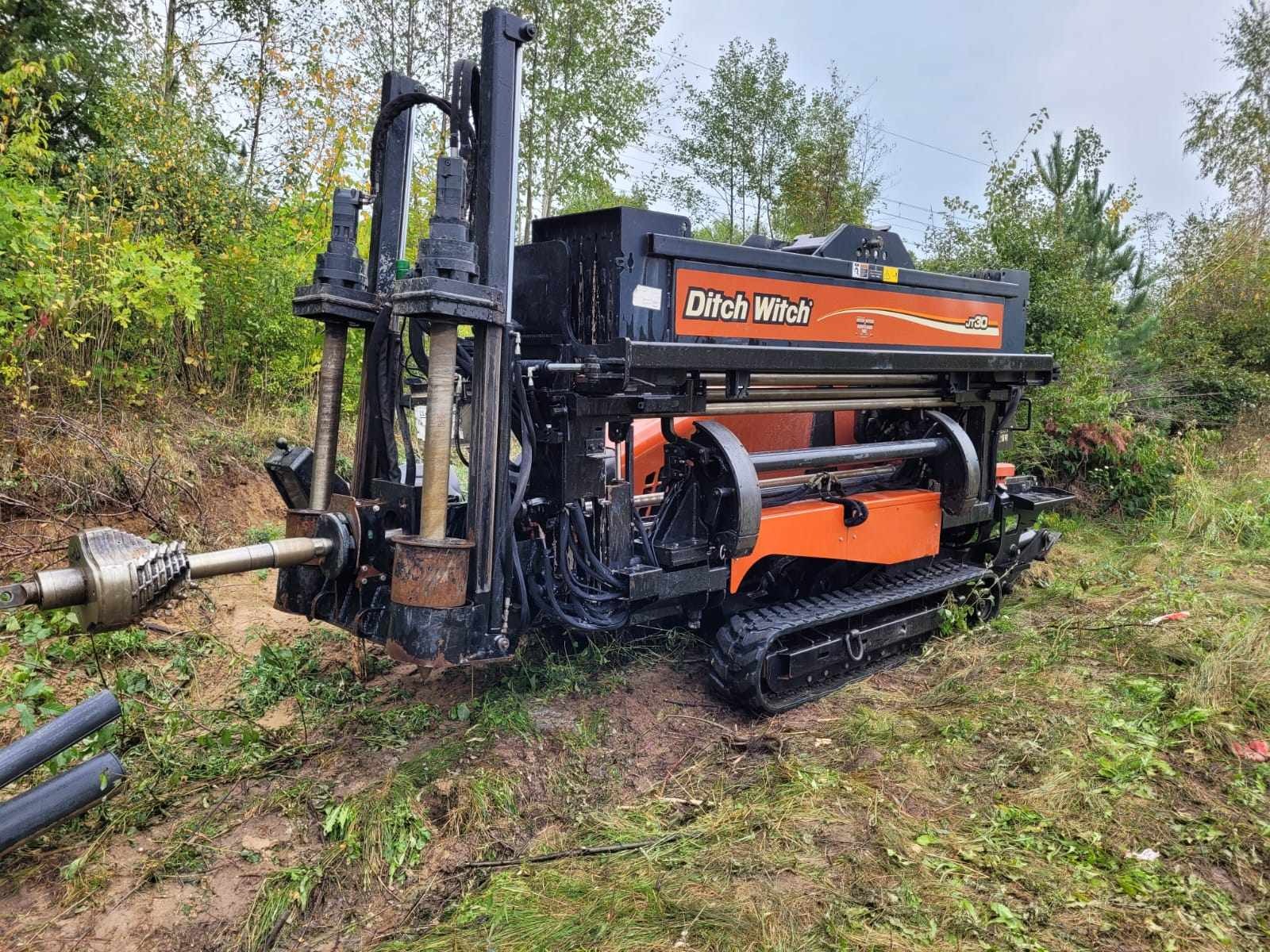 Pomarańczowo-czarna wiertnica kierunkowa Ditch Witch JT30 na gąsienicach, przygotowana do pracy na zewnątrz; widoczne przewody rurowe i błotniste podłoże.