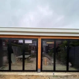 Nowoczesne, składane drzwi tarasowe z czarnymi ramami i drewnianą konstrukcją w trakcie montażu we Wrocławiu, widoczne narzędzia i materiały budowlane w tle.