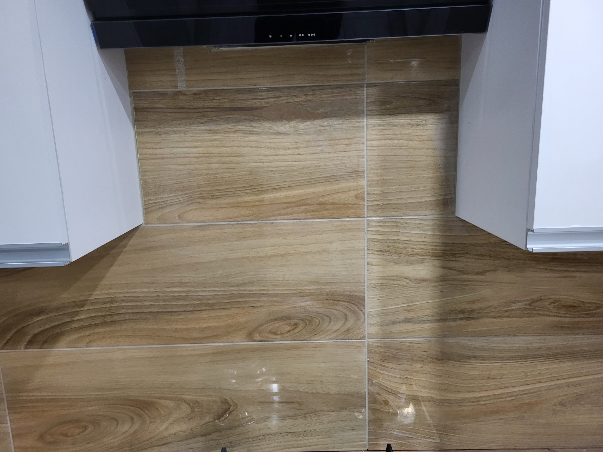 Płytki imitujące drewno na ścianie nad blatem kuchennym, pomiędzy białymi szafkami, z widocznym okapem.