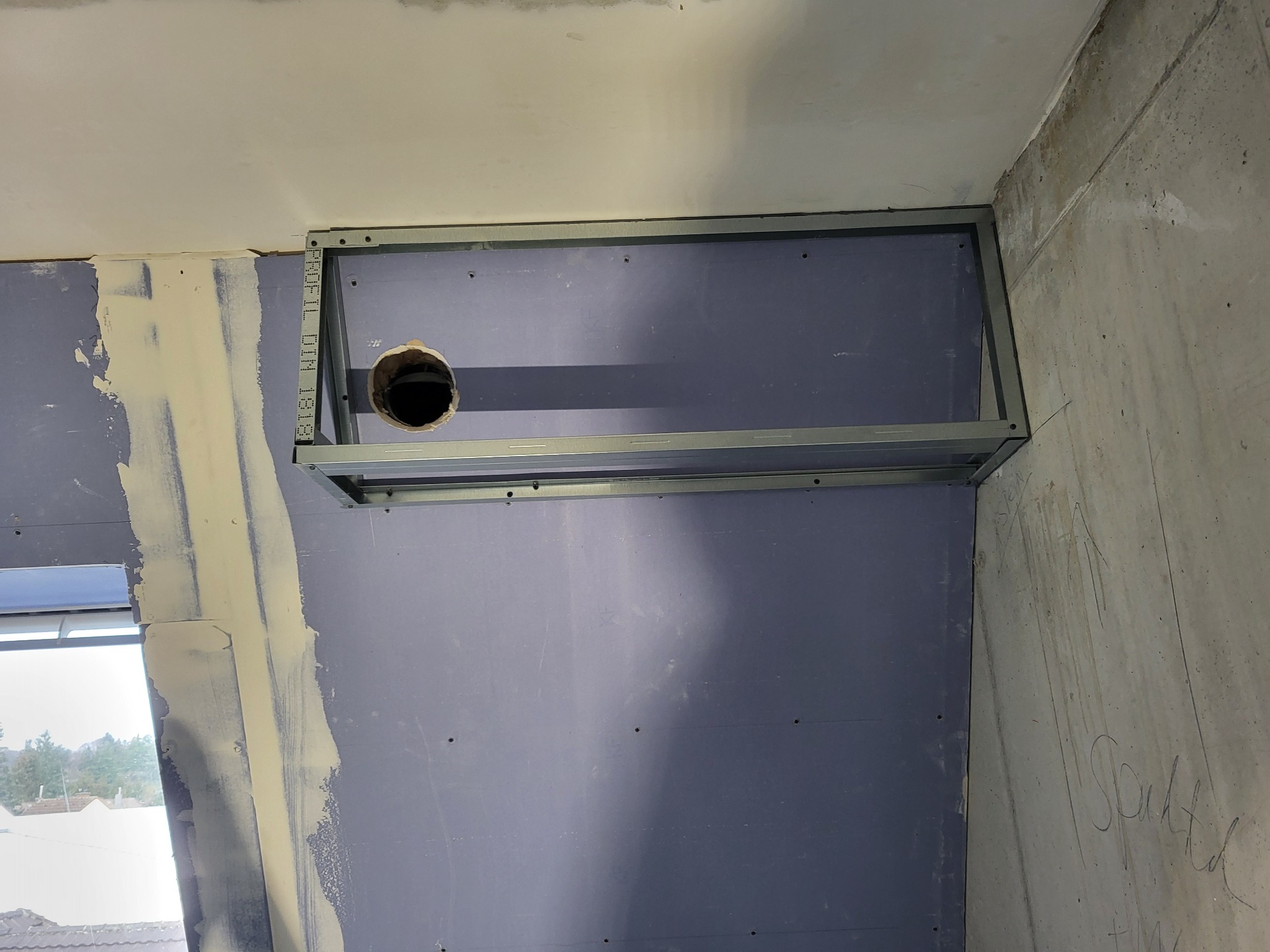 Montaż konstrukcji z profili stalowych pod płytę gipsowo-kartonową z wyciętym otworem na instalację, widoczne szpachlowanie przy oknie.