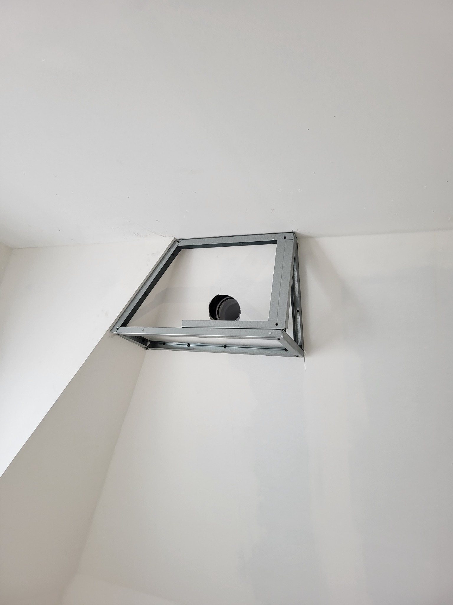 Metalowa konstrukcja pod sufit napinany z widocznym otworem wentylacyjnym w narożniku pomieszczenia o białych ścianach.