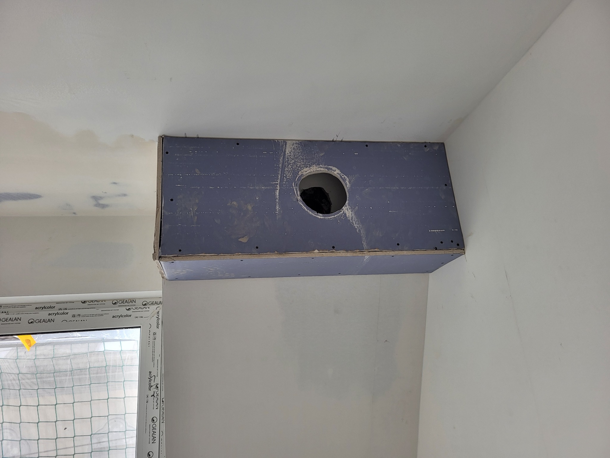 Fragment wnętrza w trakcie prac wykończeniowych: zamontowana konstrukcja z płyt kartonowo-gipsowych z otworem, surowy sufit z widocznymi śladami szpachlowania, nowe okno z profilem Gealan.