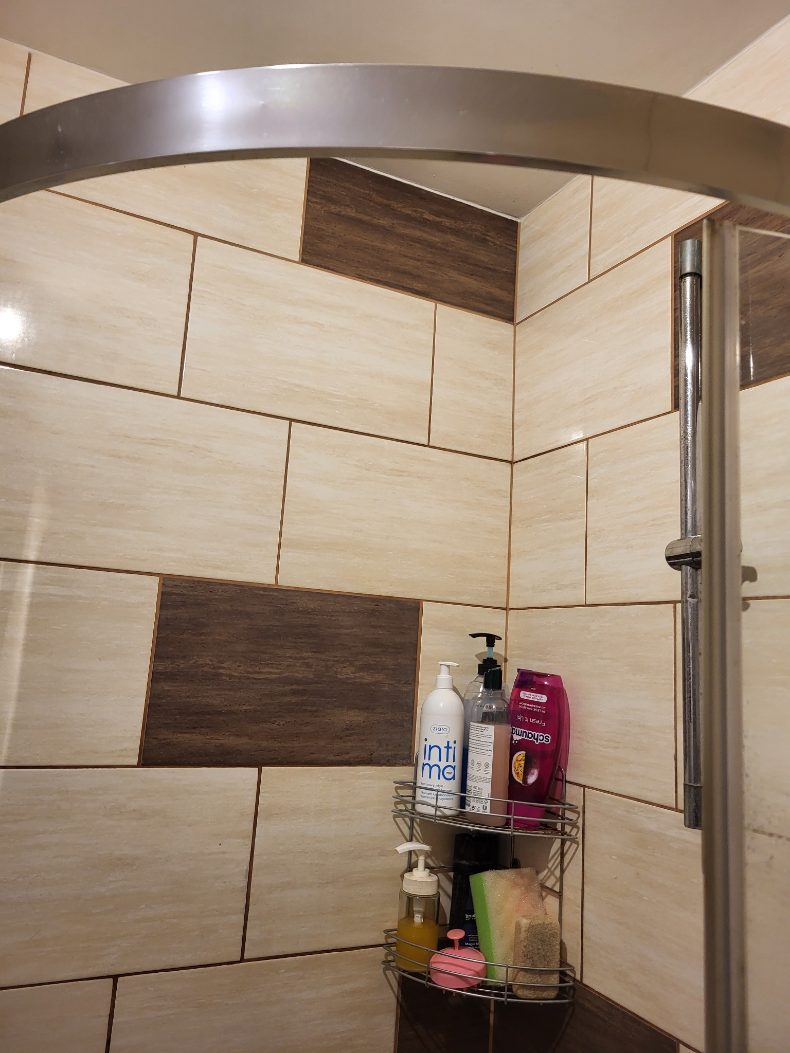 Wykończona kabina prysznicowa z beżowymi i brązowymi płytkami, metalową ramą i półką narożną z kosmetykami.