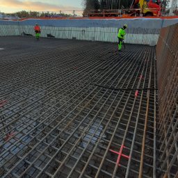 CBT BUILDING - Siatka zbrojeniowa fundamentu z widocznymi pracownikami w odblaskowych ubraniach i dźwigiem w tle.