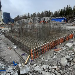 CBT BUILDING - Zbrojenie fundamentu z szalunkiem systemowym na placu budowy, w tle skały i zbiorniki przemysłowe.