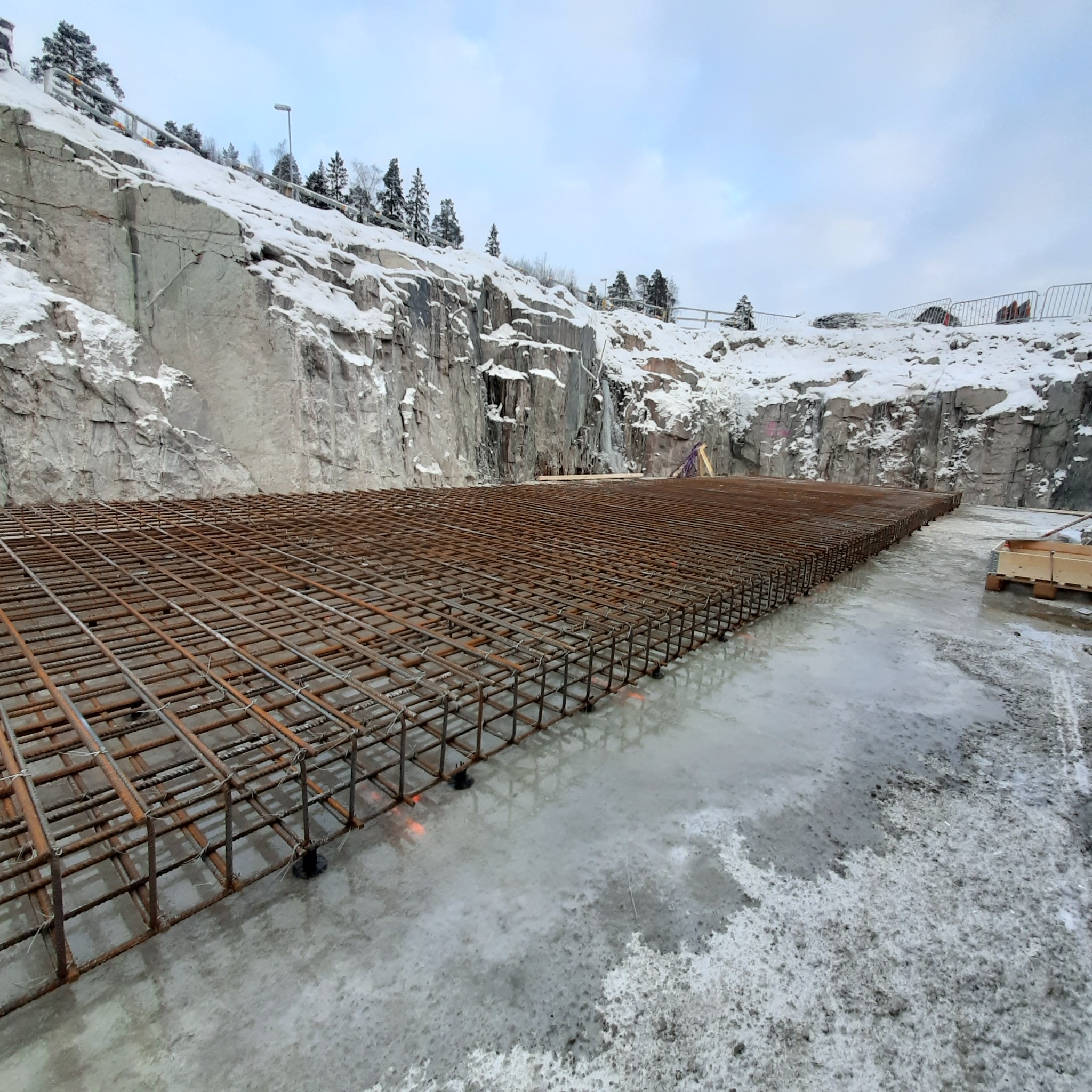 Siatka zbrojeniowa ułożona na fundamencie w zimowej scenerii, widoczne podpory dystansowe, w tle skalna ściana pokryta śniegiem.