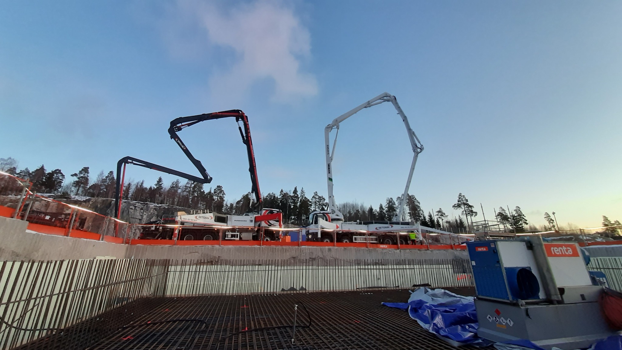 Przygotowanie zbrojenia fundamentów pod budowę, z widocznymi dwiema pompami do betonu na tle drzew i nieba.