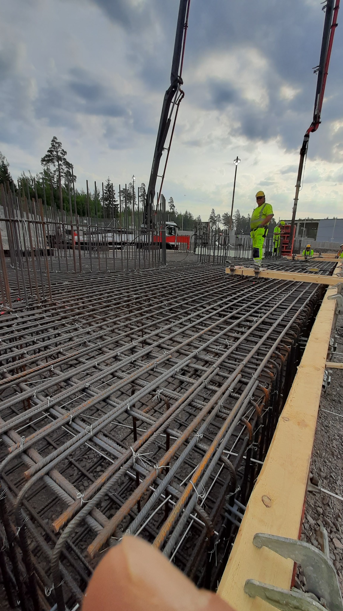 Siatka zbrojeniowa fundamentu przygotowana do zalewania betonem, widoczni pracownicy w odblaskowych ubraniach i pompy do betonu w tle.