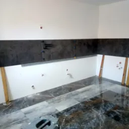 Montaż ciemnych płytek na ścianie w kuchni, widoczne drewniane podpory, poziomica i krzyżyki dystansowe, podłoga wyłożona błyszczącymi płytkami imitującymi marmur.