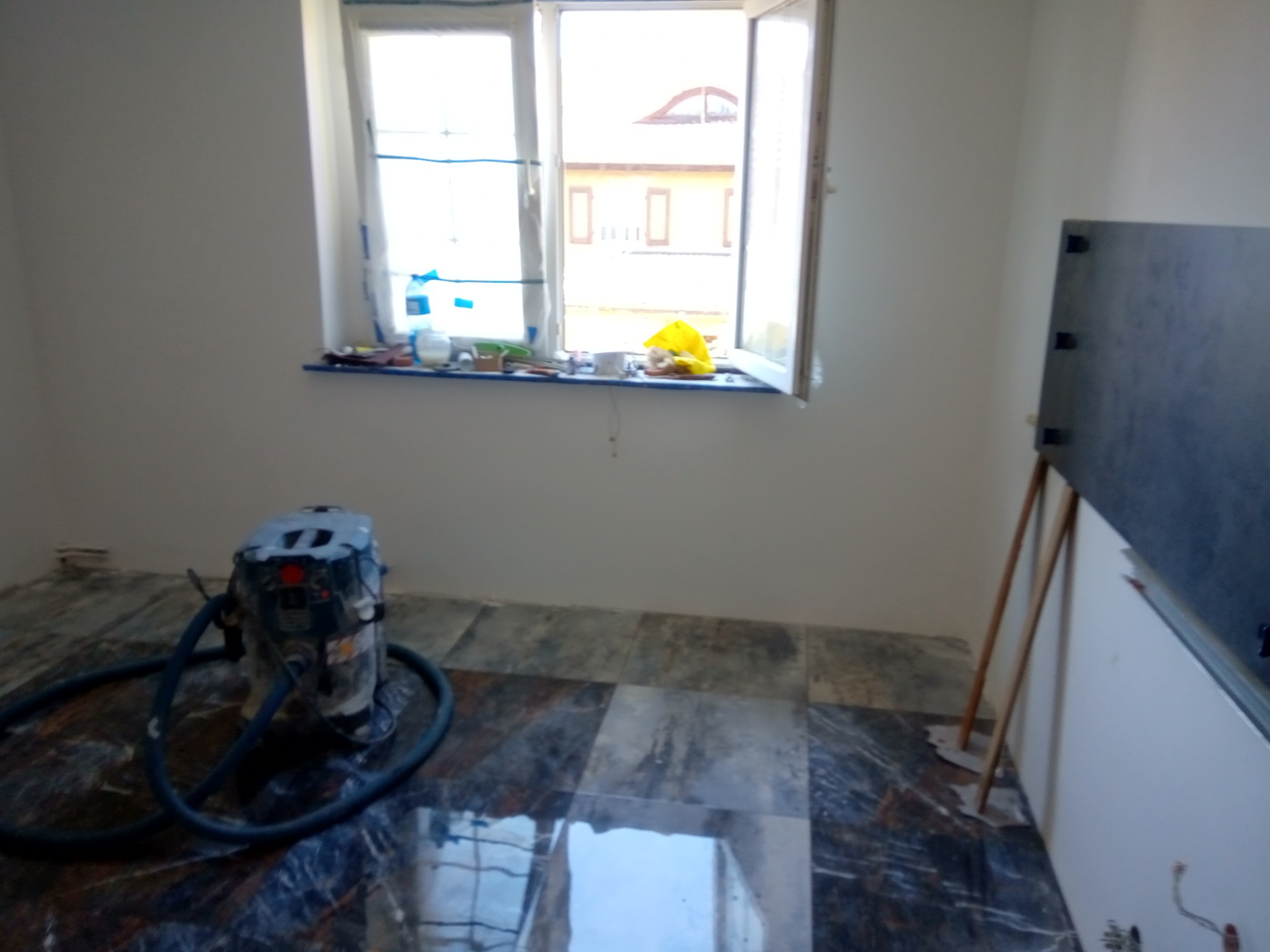 Wnętrze pokoju w trakcie remontu z odkurzaczem przemysłowym na marmurowej podłodze i profilem przy ścianie.