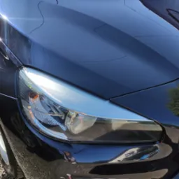 Błyszczący, czarny samochód po umyciu w Opolu, widoczny reflektor i fragment maski z odbiciami otoczenia.