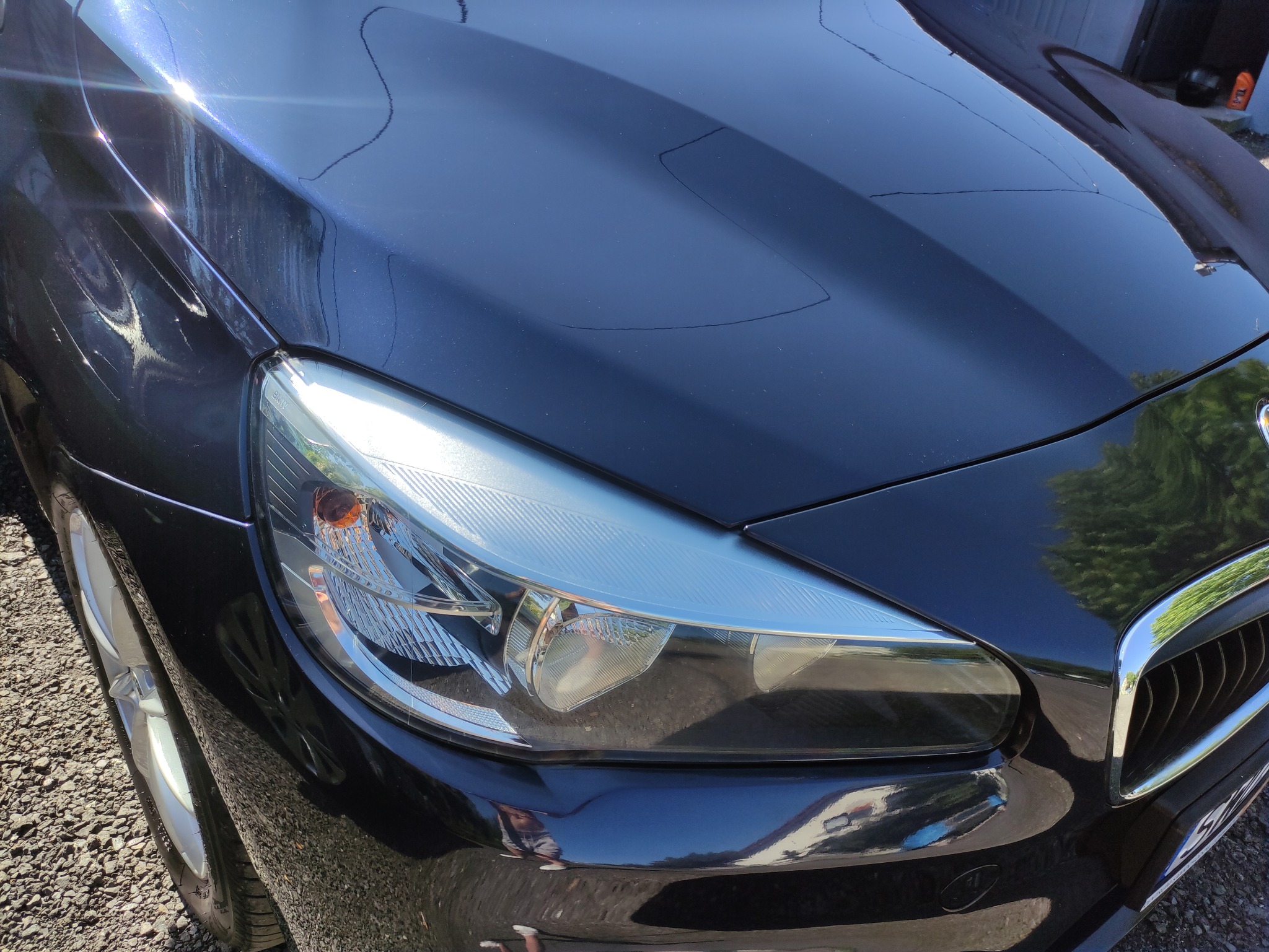 Błyszczący, czarny samochód po umyciu w Opolu, widoczny reflektor i fragment maski z odbiciami otoczenia.