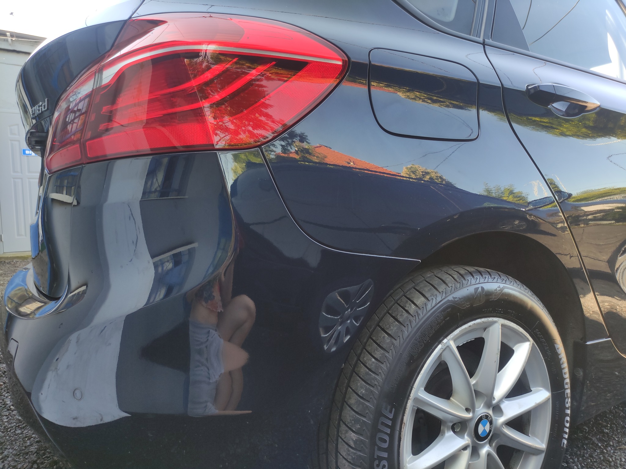 Błyszczący, granatowy samochód BMW po umyciu, widoczny tylny reflektor, opona z felgą aluminiową oraz odbicie otoczenia w lakierze.