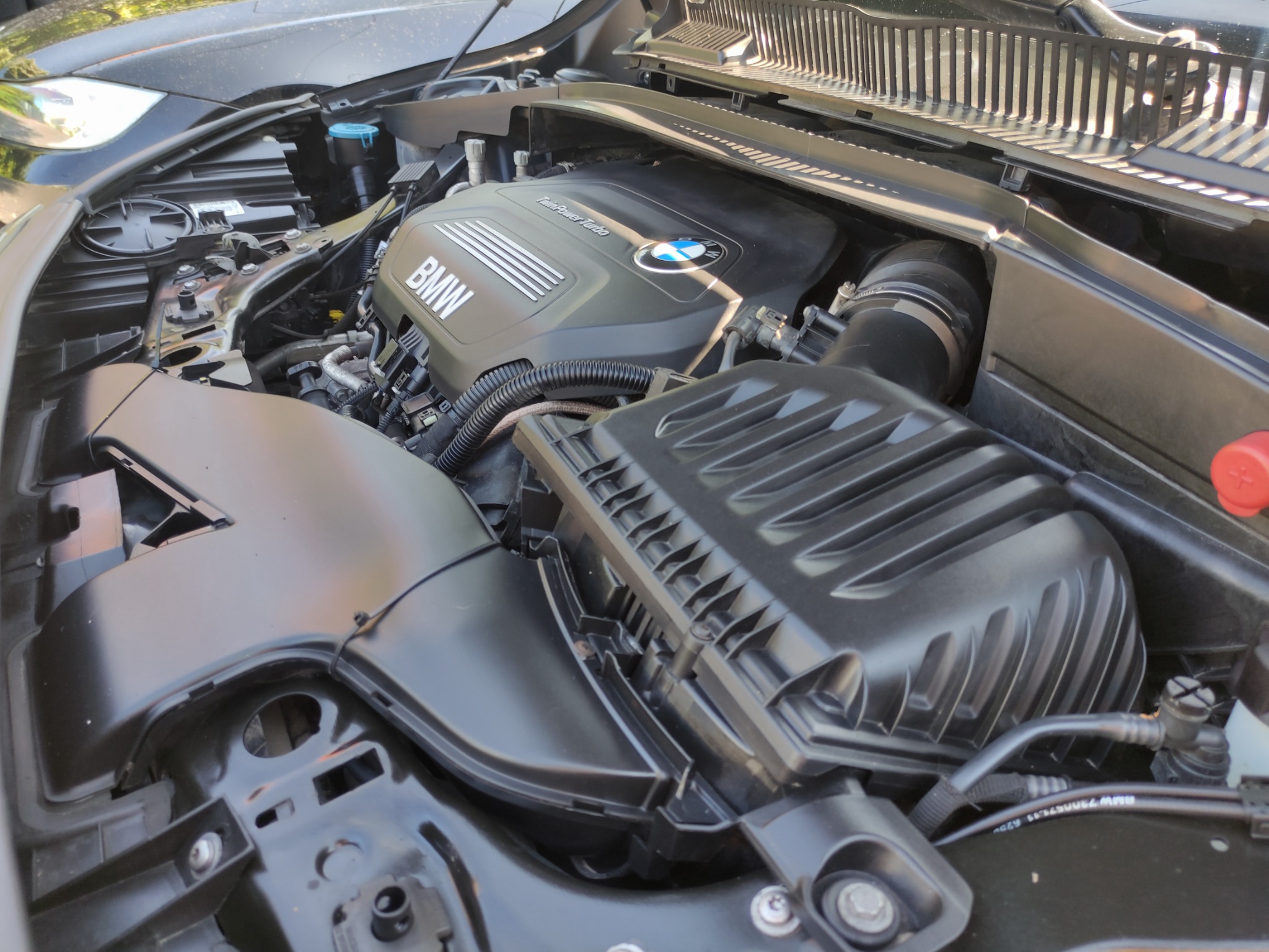 Otwarta maska samochodu BMW, widoczny silnik Twin Power Turbo z elementami osprzętu, przewody i zbiorniczki płynów eksploatacyjnych.