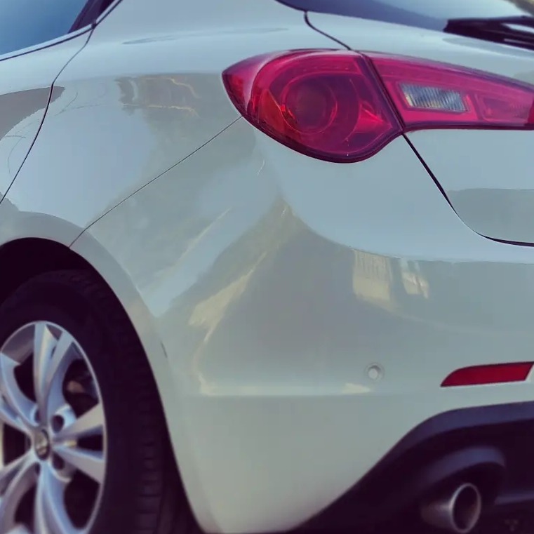 Biały samochód osobowy, widok z tyłu, z widocznym światłem stop, felgą i końcówką wydechu. Lakier po polerowaniu z wyraźnymi refleksami światła.