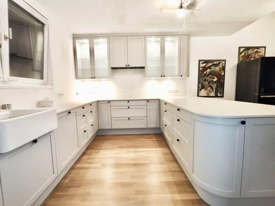 Jasna kuchnia na wymiar w kształcie litery U z drewnianą podłogą, ceramicznym zlewem i wiszącymi szafkami z podświetleniem LED.