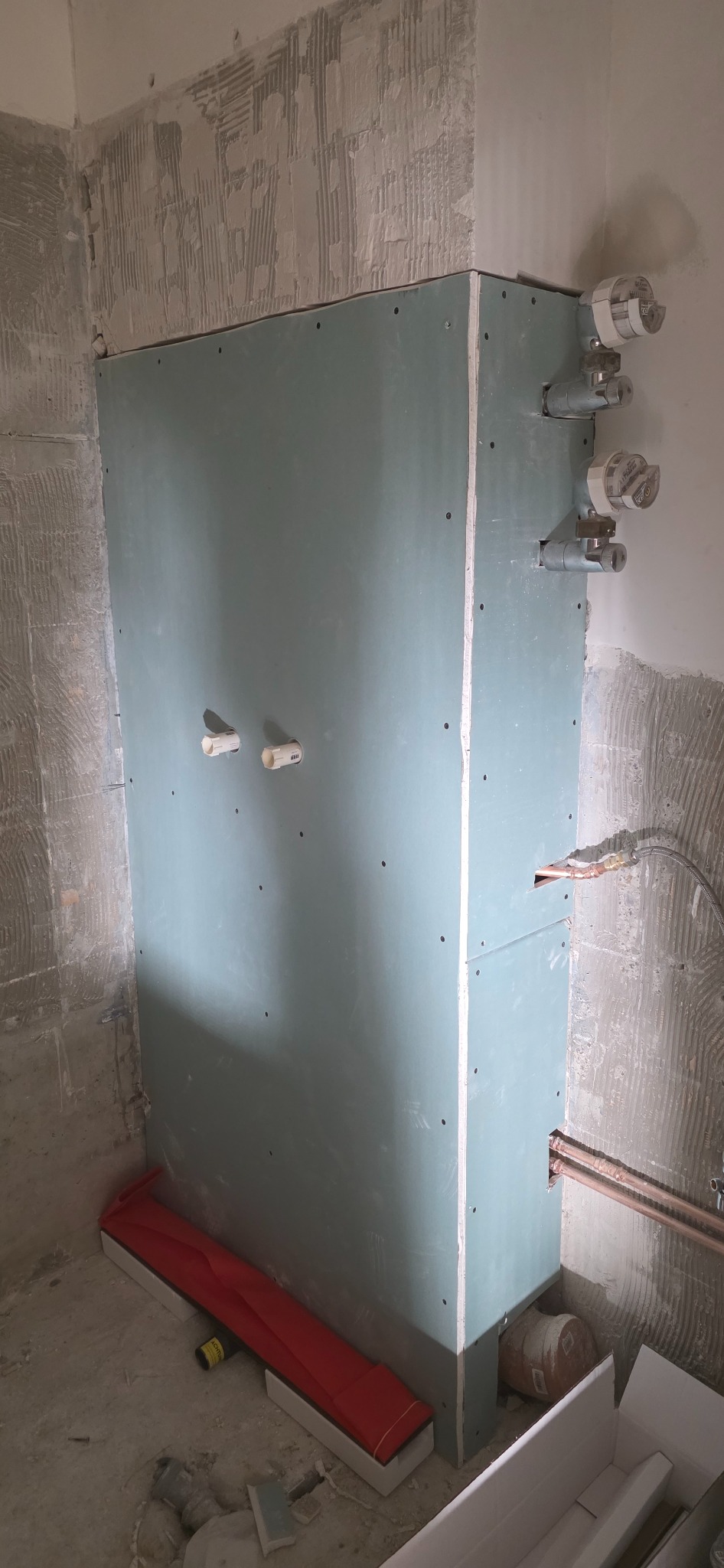 Ścianka z płyt gipsowo-kartonowych w łazience w trakcie remontu, widoczne rury i instalacje wodne. Surowy stan ścian, przygotowanie do wykończenia.