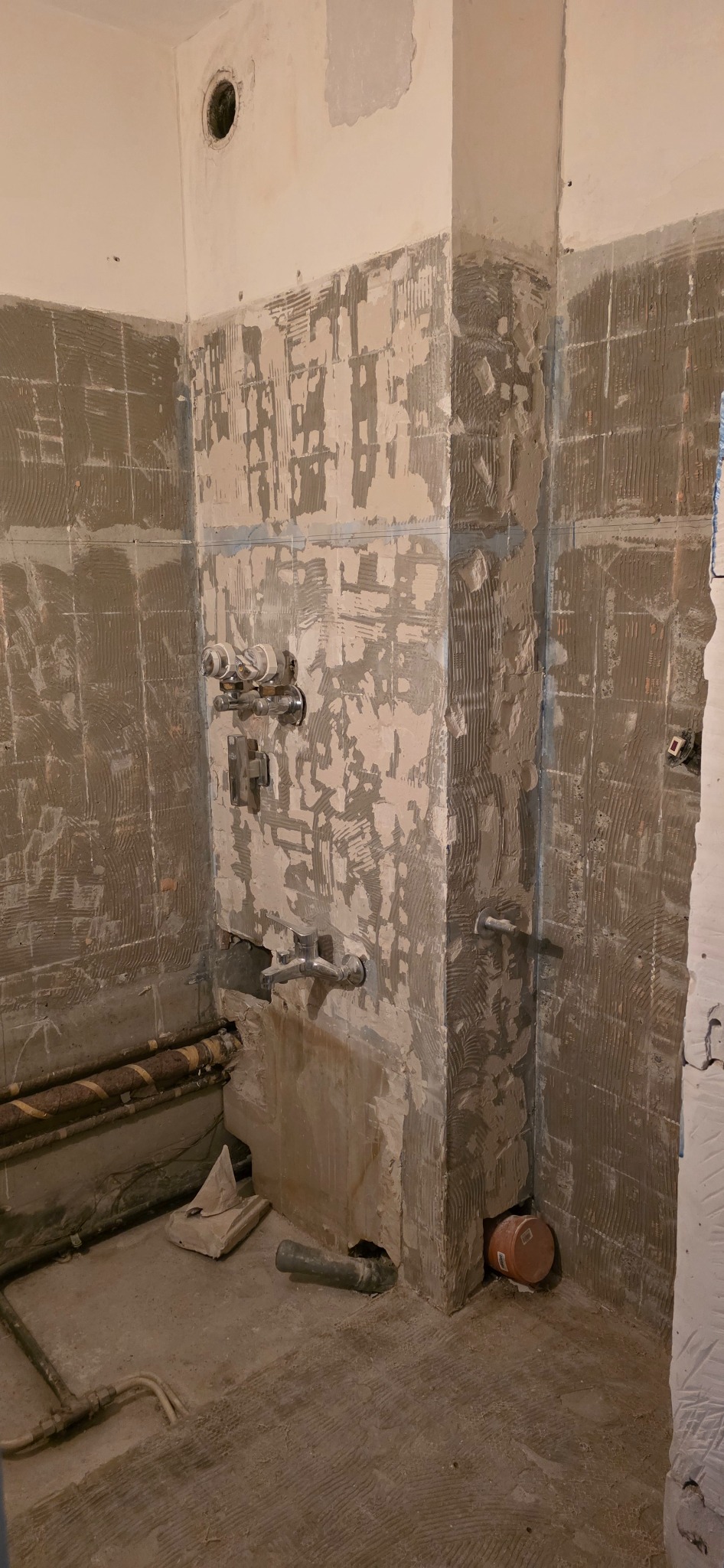 Łazienka w trakcie remontu: ściany z resztkami płytek i kleju, widoczne rury i instalacje wodne. Przygotowanie do dalszych prac wykończeniowych.