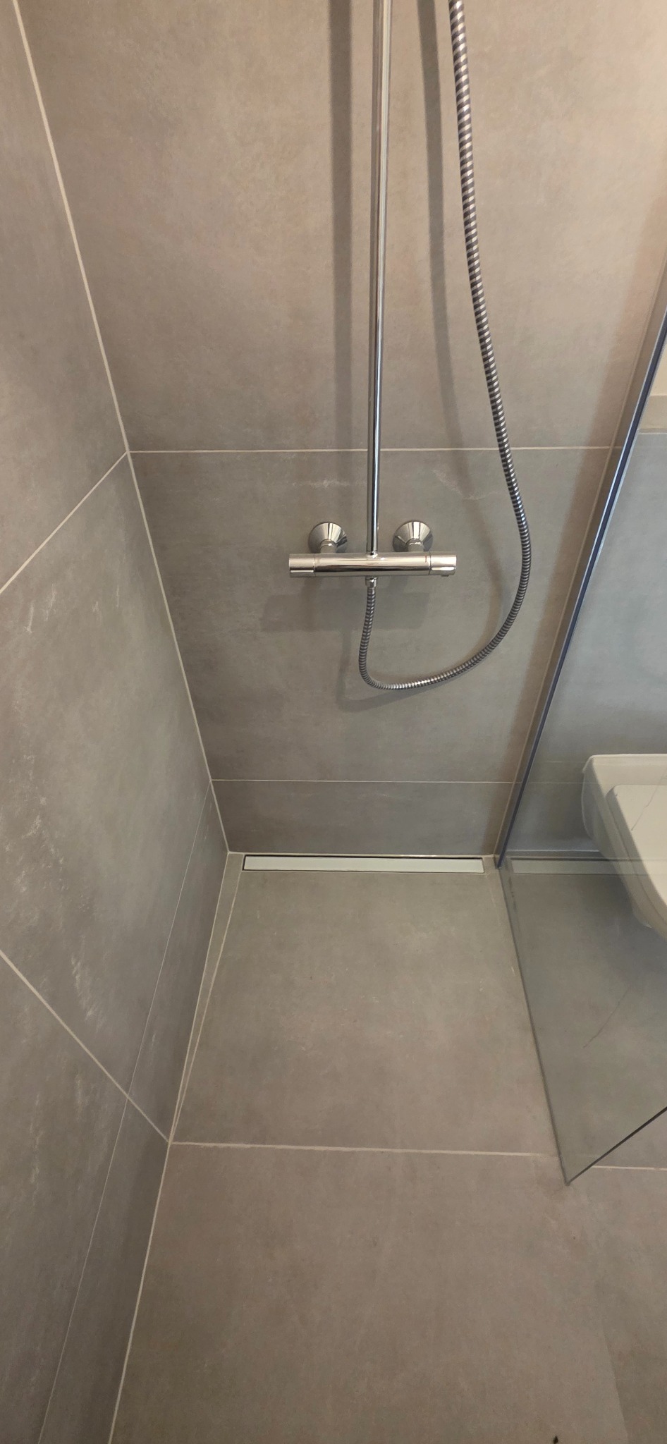 Szare płytki w nowoczesnej kabinie prysznicowej z odpływem liniowym i chromowaną armaturą. Minimalistyczny design, widok z góry.