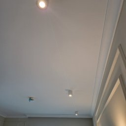 Mianatura sp. Z o.o. - Biały sufit z zamontowanymi trzema cylindrycznymi lampami LED, widoczna listwa dekoracyjna przy ścianie i zabezpieczony czujnik dymu na suficie.