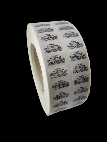 Rolka przezroczystych etykiet samoprzylepnych z nadrukowanym czarnym tekstem i kalendarzem, skierowana pod kątem na czarnym tle.