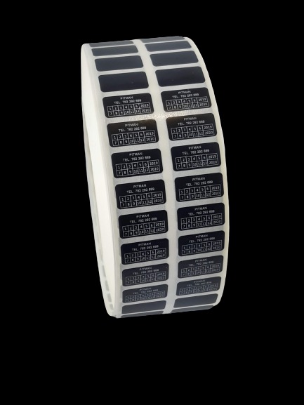 Rolka czarnych, prostokątnych etykiet z kalendarzem, numerem telefonu i nazwą 'PITMAN' na białym podkładzie, widoczne z bliska na czarnym tle.