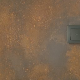 ANTIGUS Adrian KLUCZNY - Szary włącznik światła z ikoną żarówki na ścianie o dekoracyjnej, rdzawobrązowej fakturze. Minimalistyczny design w nowoczesnym wnętrzu.