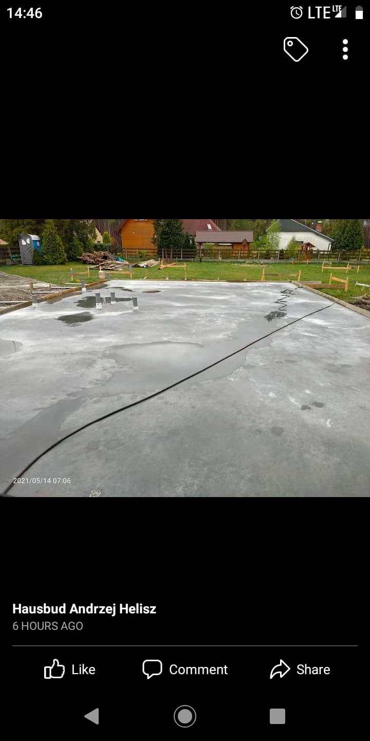 Świeżo wylany beton fundamentowy z widocznymi rurami instalacyjnymi i drewnianym szalunkiem obwodowym, niewielkie kałuże na powierzchni betonu.