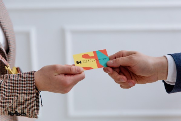 Wymiana wizytówki Salonu Nieruchomości między dwiema osobami w eleganckich marynarkach, na jasnym tle.