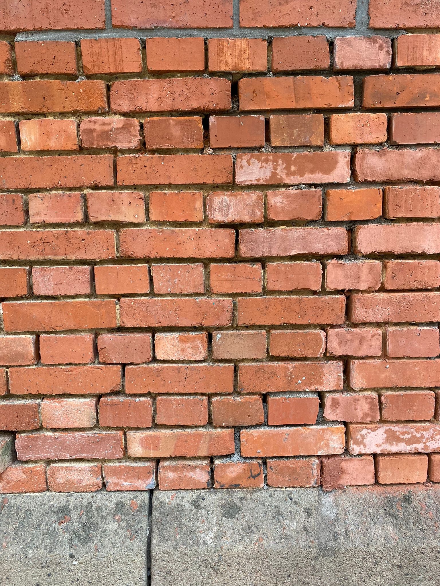 Fragment muru z czerwonej cegły z widocznymi spoinami i betonową podstawą, ukazujący teksturę i detale materiałów budowlanych.