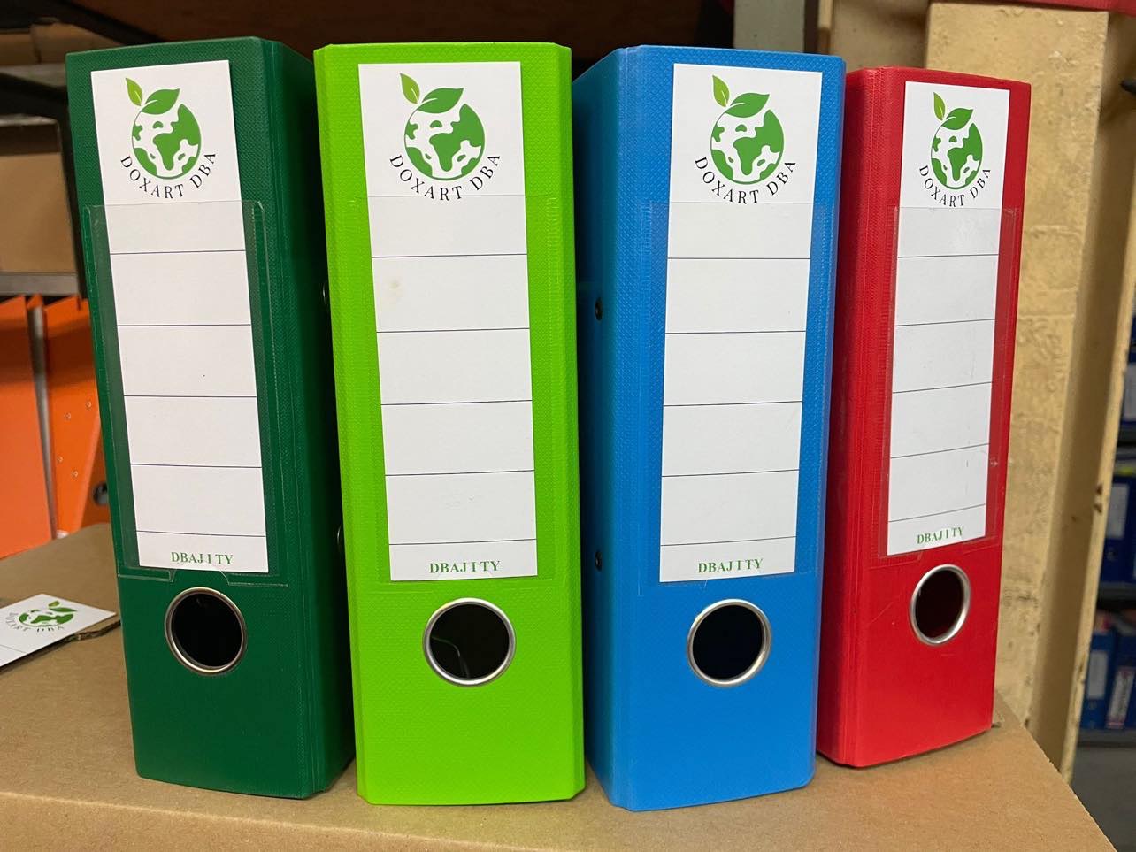 Kolorowe segregatory firmowe (zielony, limonkowy, niebieski, czerwony) z logo DOXART DBAJITY, ustawione w rzędzie, prezentujące archiwizację dokumentów.